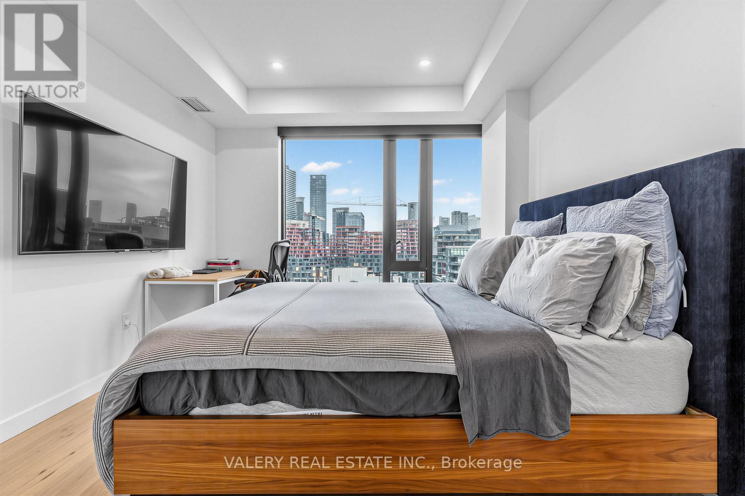 A bedroom with a large bed and a city view through the window.