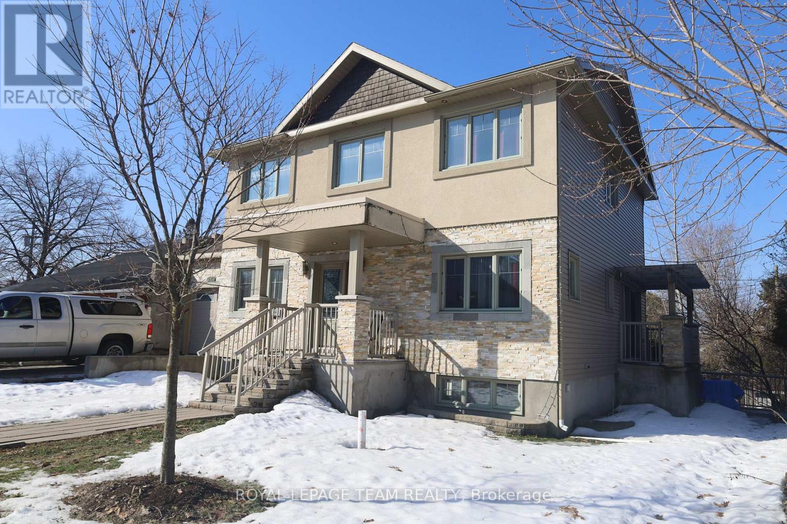 A house with a brown roof and a grey exterior is shown with snow on the ground.