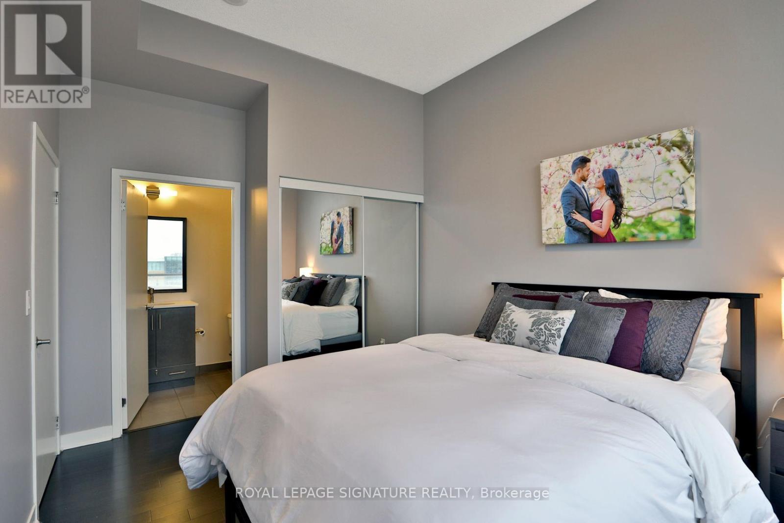 A bedroom with a large bed and a painting of a couple on the wall.