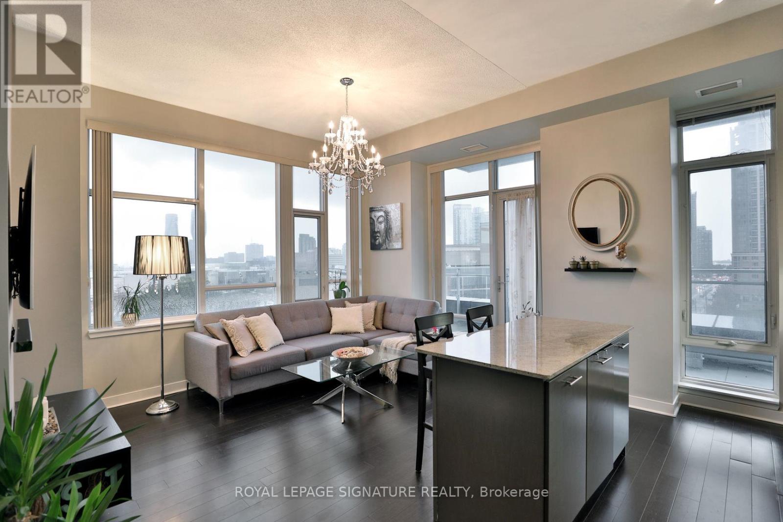 A well-lit, spacious living room with a grey sofa and a chandelier.
