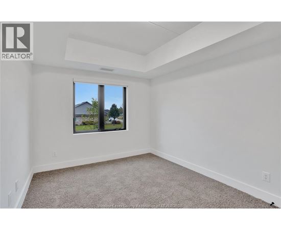 A white room with a carpeted floor and a window showing a view of a house and trees.