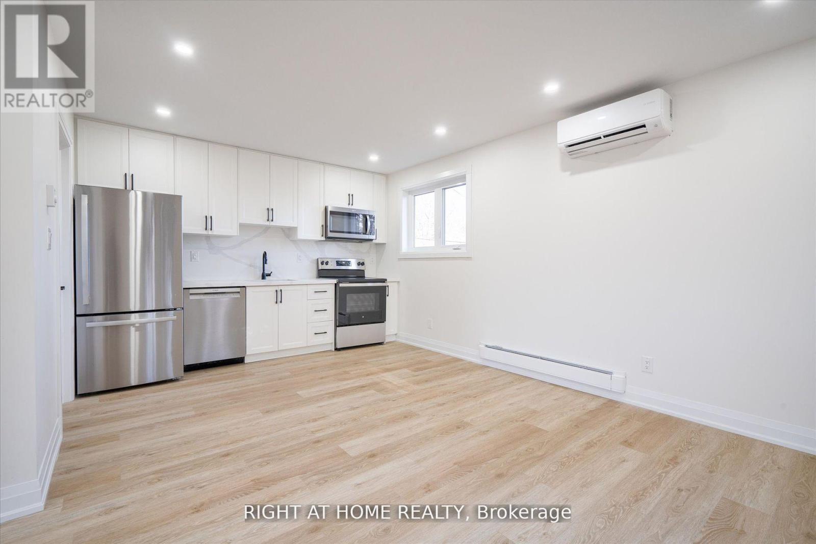 A white kitchen with wooden floors and stainless steel appliances.