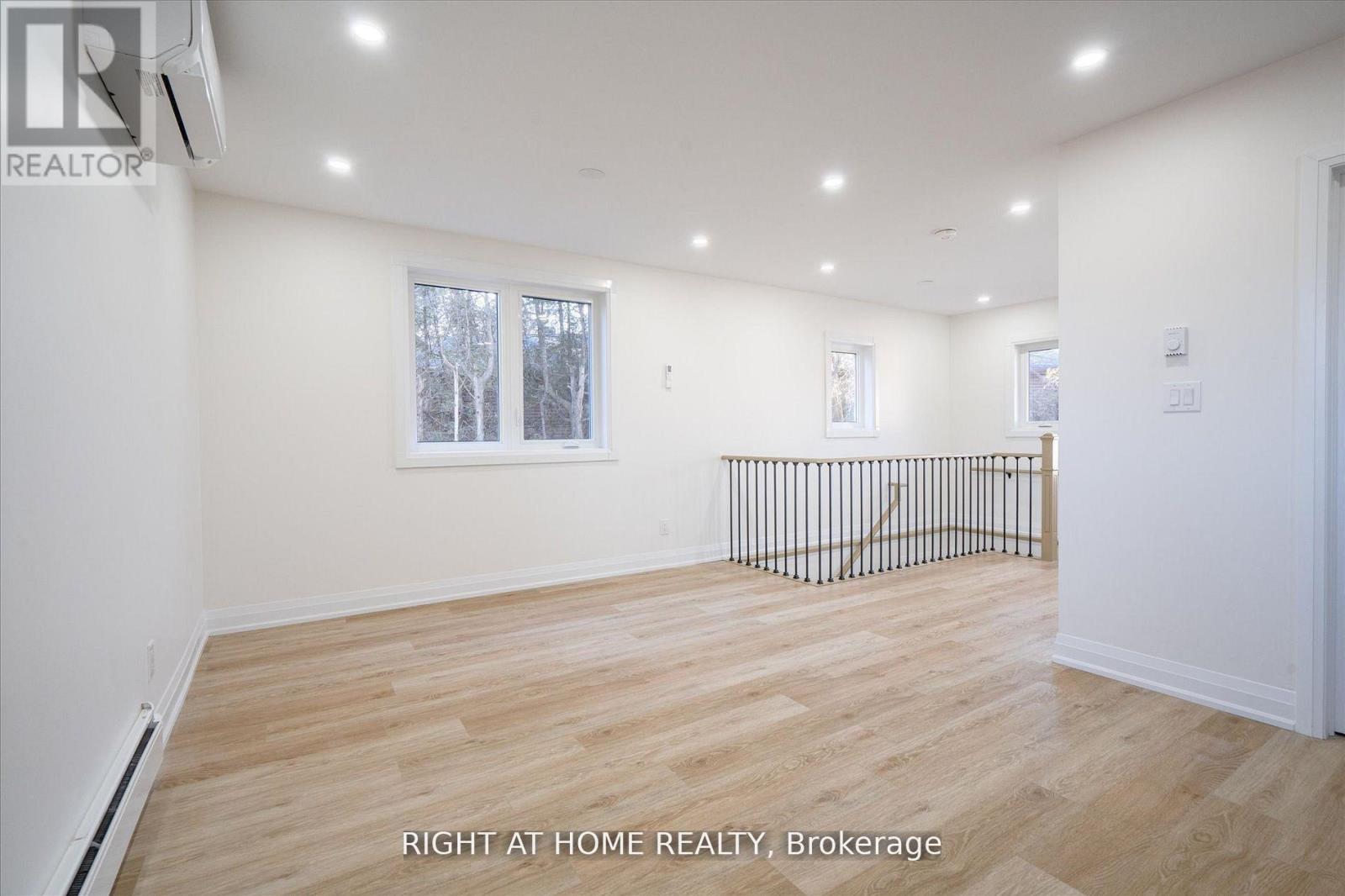 A spacious room with wooden flooring and white walls, with a window and a metal railing.