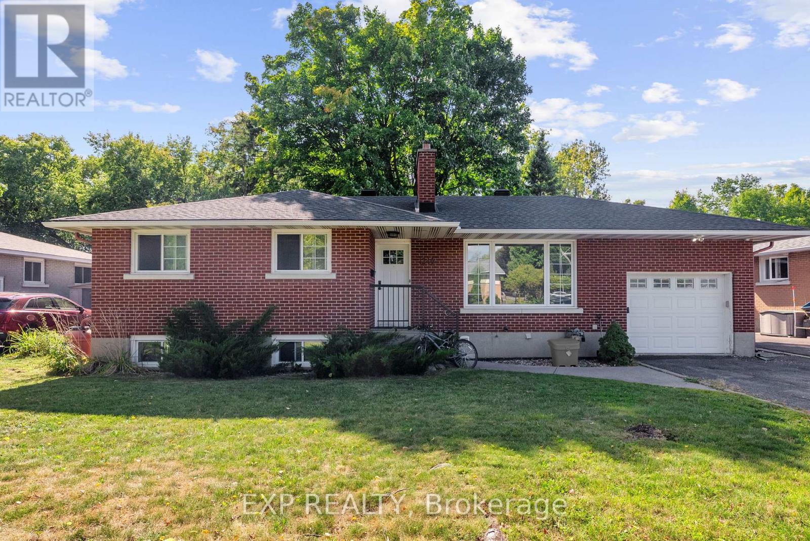 A red brick house with a white garage door and a tree in the front yard.