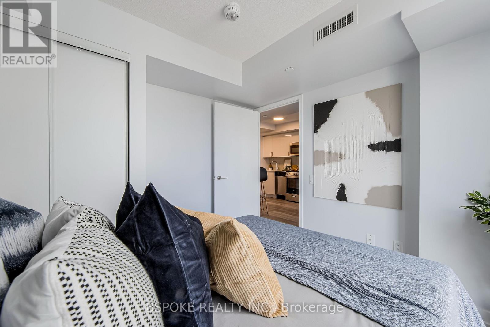 A bedroom with a bed and pillows in the foreground and a hallway with a doorway leading to another room in the background.
