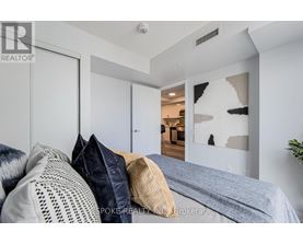 A bedroom with a bed and pillows in the foreground and a hallway with a doorway leading to another room in the background.