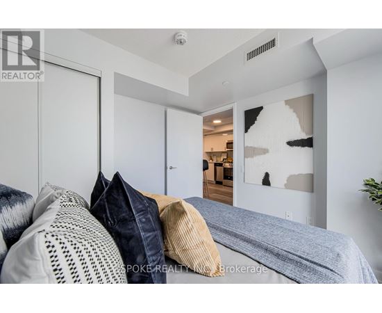 A bedroom with a bed and pillows in the foreground and a hallway with a doorway leading to another room in the background.