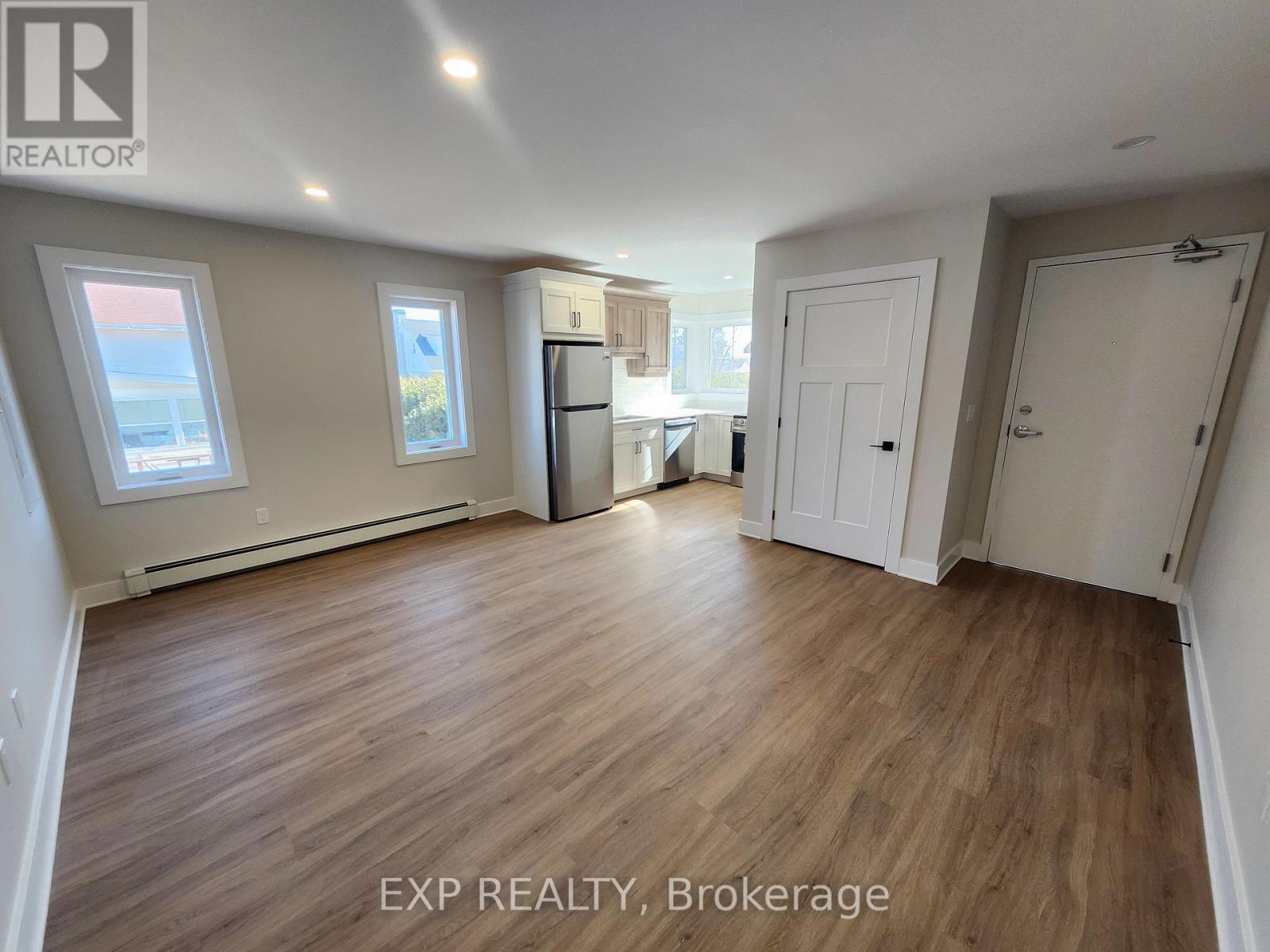 A room with wooden flooring and white walls, with a window on the left side.