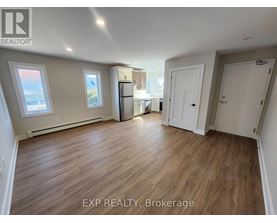 A room with wooden flooring and white walls, with a window on the left side.