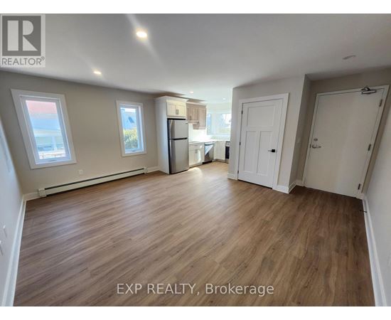 A room with wooden flooring and white walls, with a window on the left side.