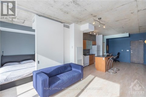 A living room with a blue couch and a bed in the background.