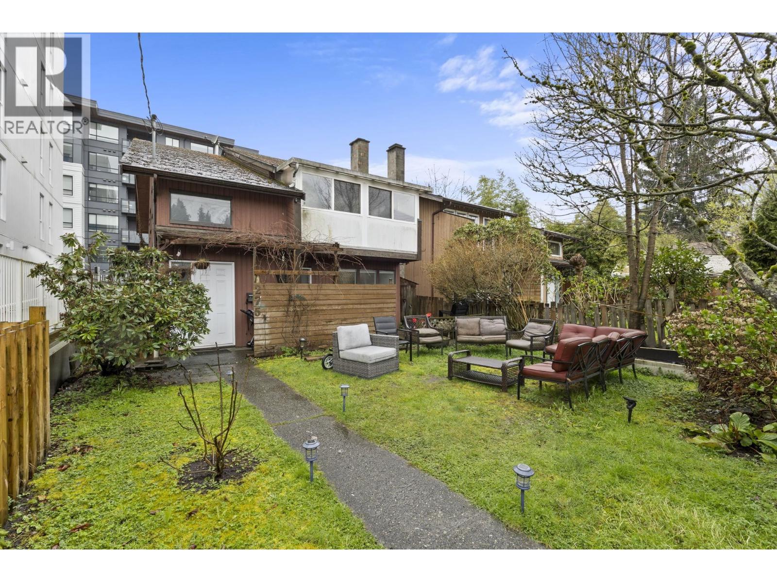 A backyard with a lawn, a small tree, and a patio with chairs and a table.