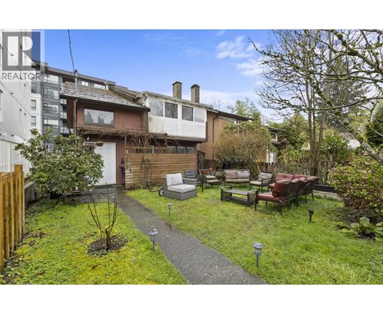 A backyard with a lawn, a small tree, and a patio with chairs and a table.