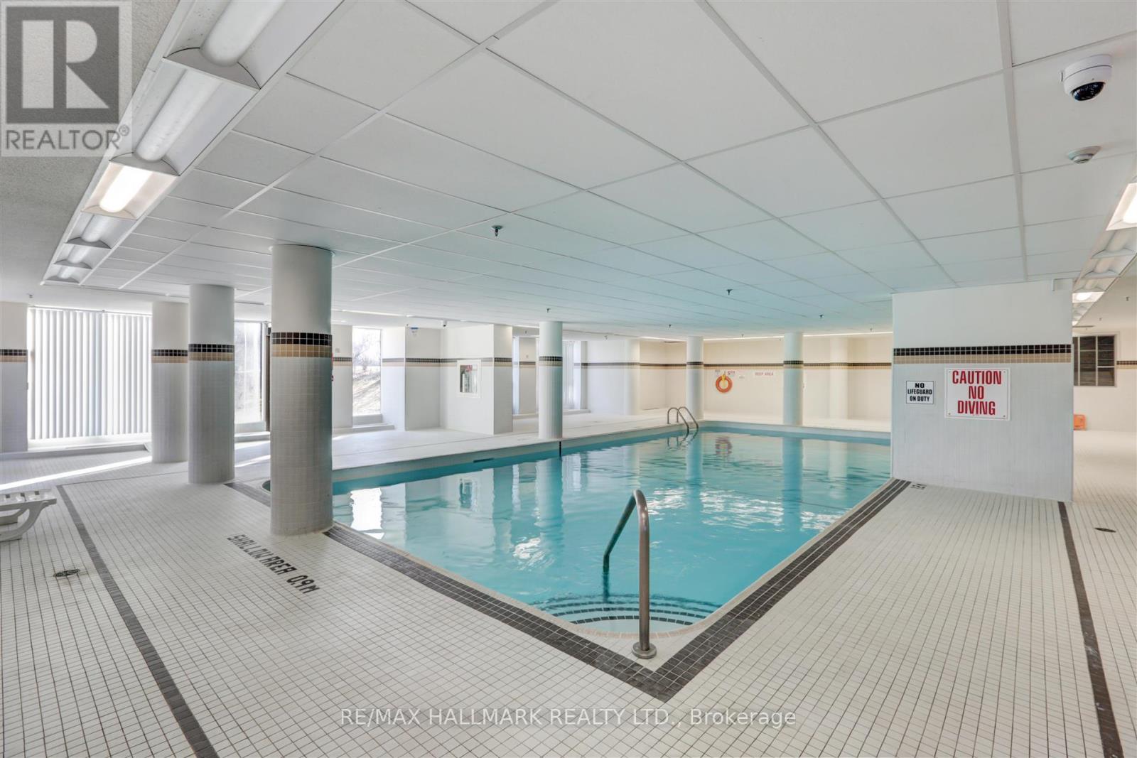 A large indoor swimming pool with a caution sign on the wall.