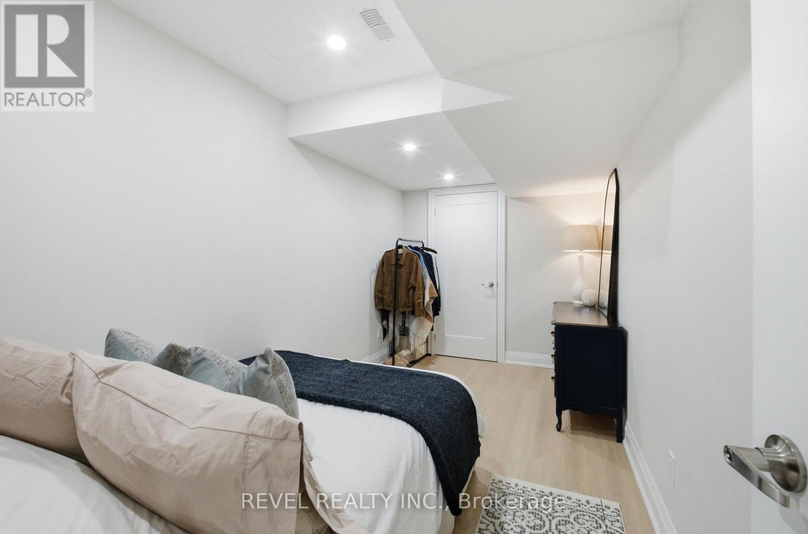 A bedroom with a bed, a coat rack, and a small table with a lamp.