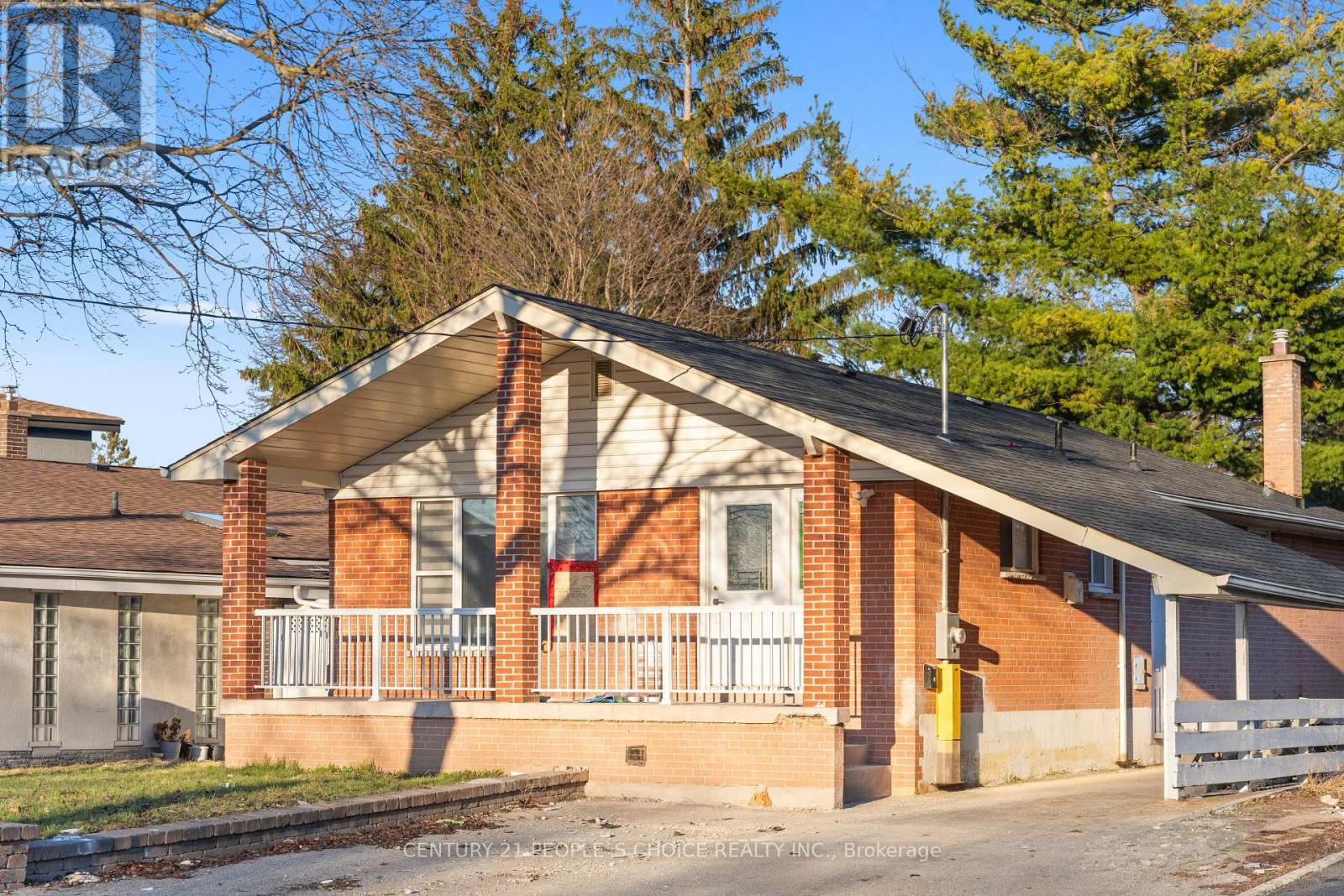 A brick house with a porch and a white fence in front.