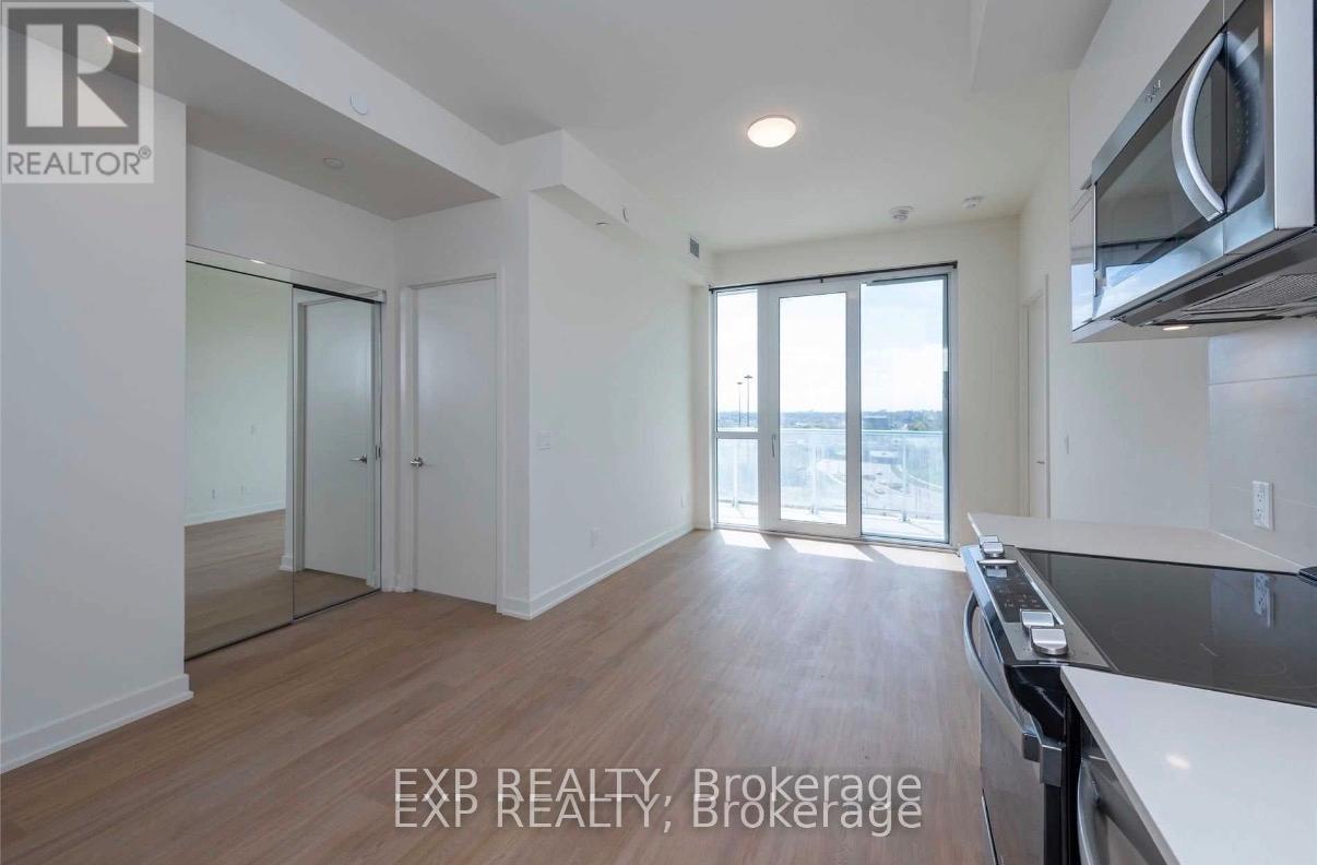 A well-lit, empty kitchen and living room with wooden floors and white walls.