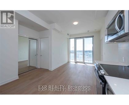 A well-lit, empty kitchen and living room with wooden floors and white walls.