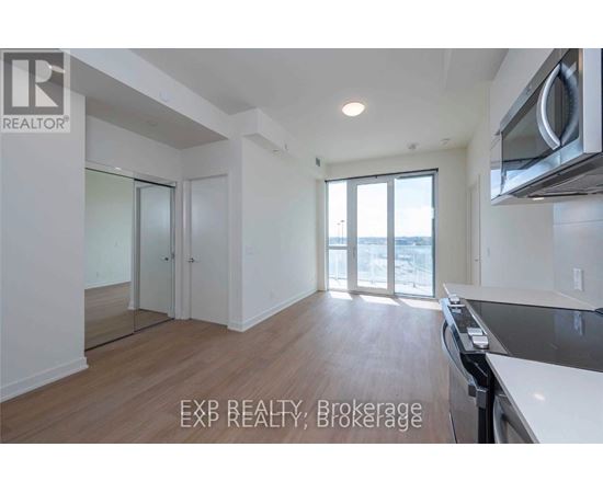 A well-lit, empty kitchen and living room with wooden floors and white walls.