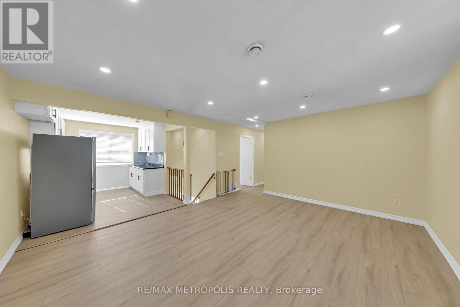 A spacious room with wooden flooring and a refrigerator in the corner.