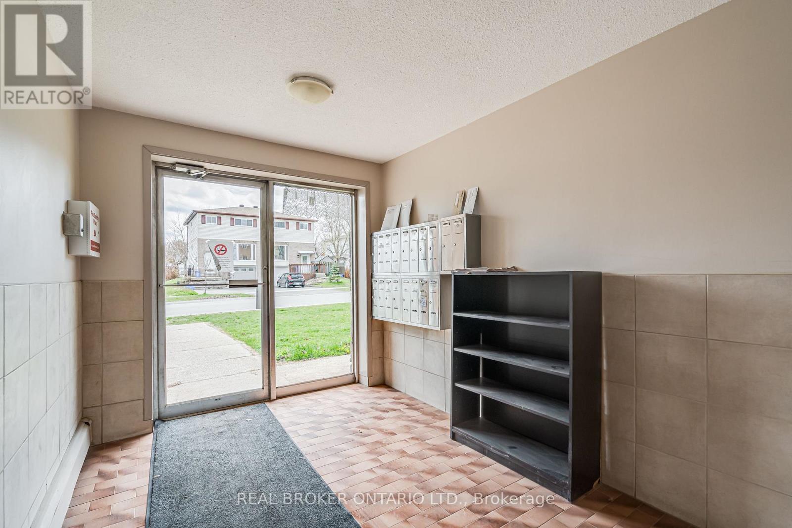 A hallway with a door leading outside and a shelf on the wall.