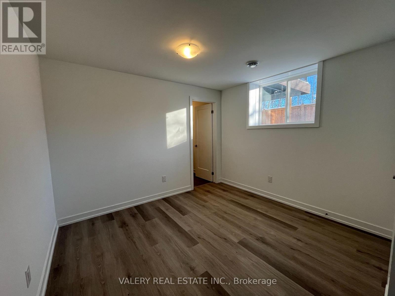 A room with wooden flooring and a window with a view of a building outside.