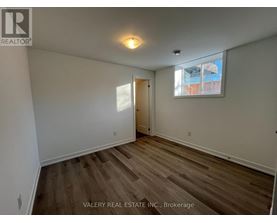 A room with wooden flooring and a window with a view of a building outside.