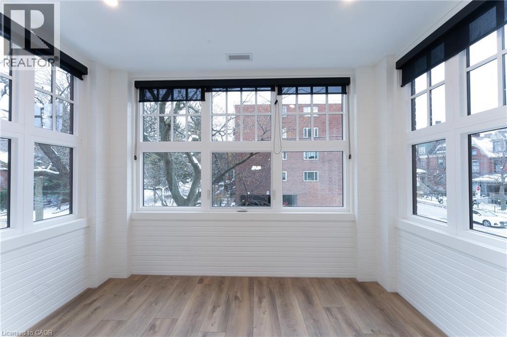 A room with white walls and wooden flooring, with a large window showing a view of a red brick building.