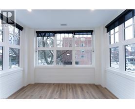 A room with white walls and wooden flooring, with a large window showing a view of a red brick building.