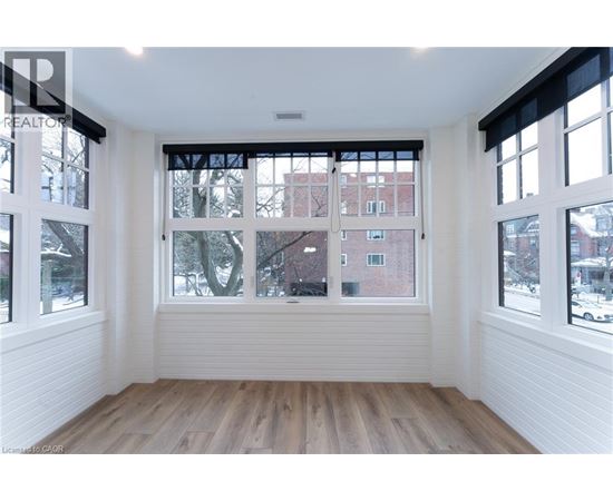 A room with white walls and wooden flooring, with a large window showing a view of a red brick building.