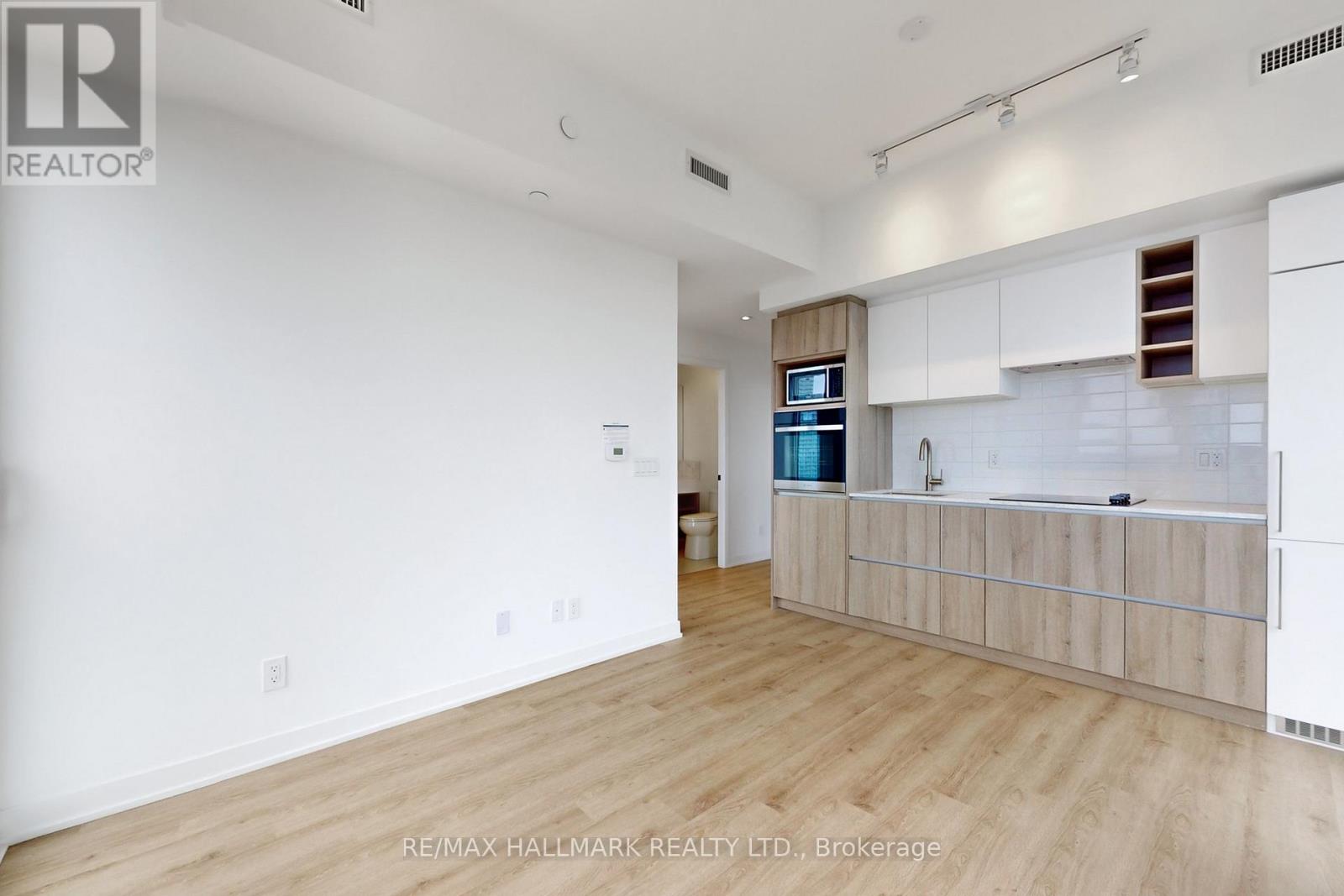 A spacious room with wooden flooring and white walls, featuring a kitchen area with white cabinets and a countertop.