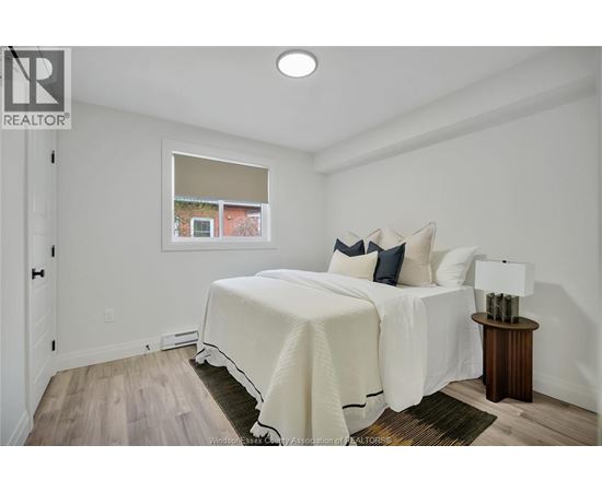 A bedroom with a white bed and a small table with a lamp.