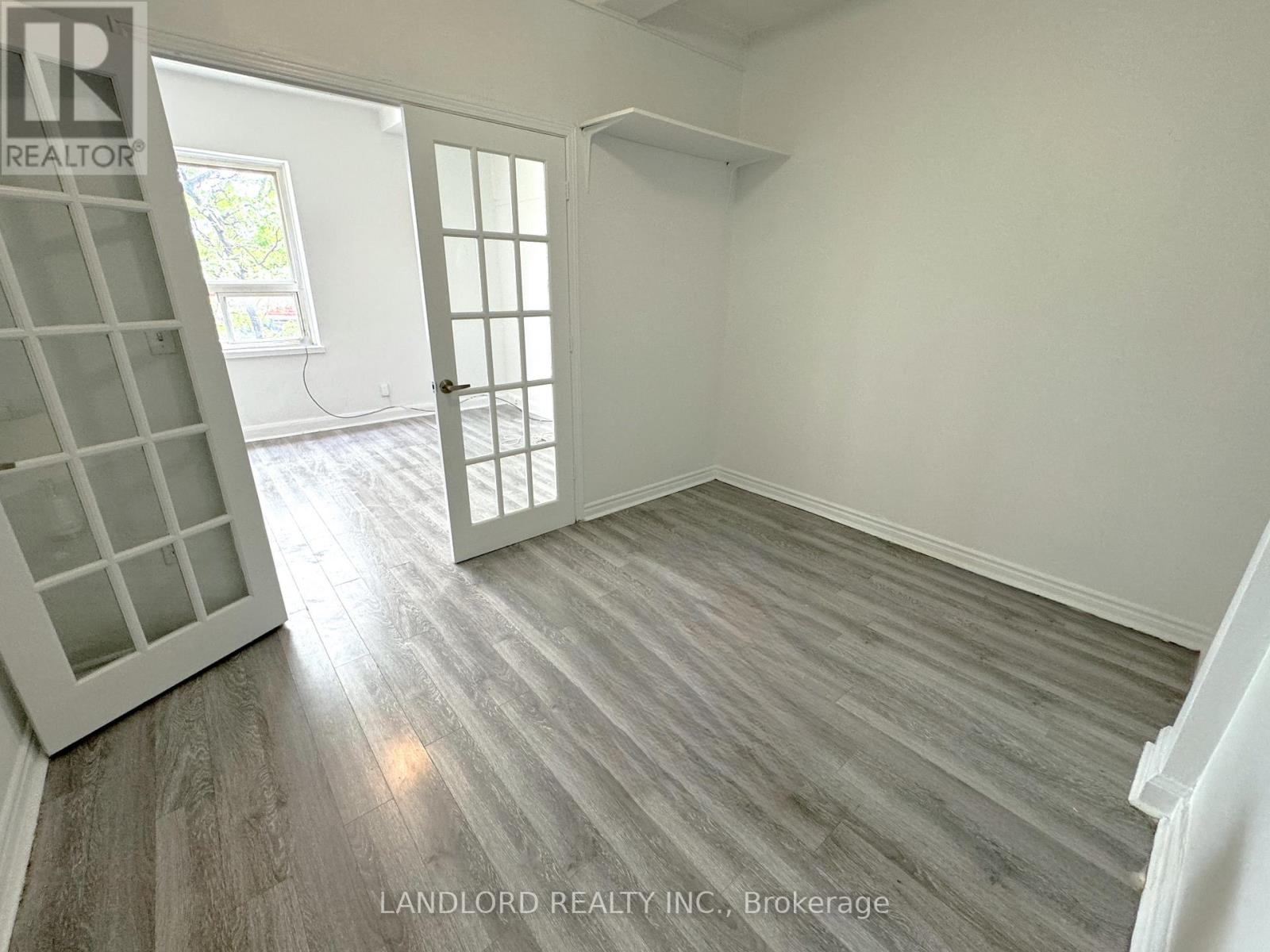A room with wooden flooring and white walls, with a window and a door visible.