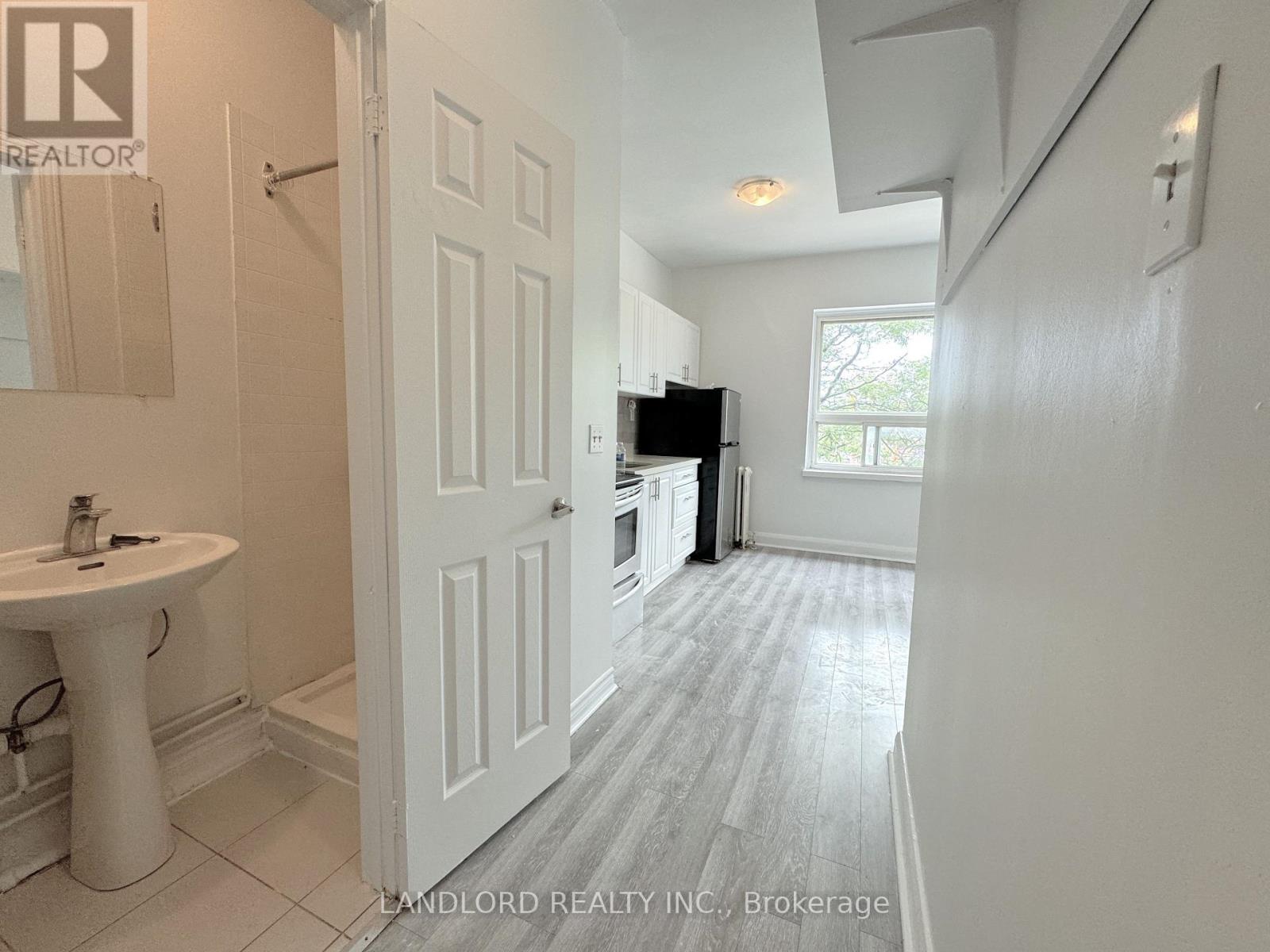 A white bathroom with a sink and a door leading to a kitchen.