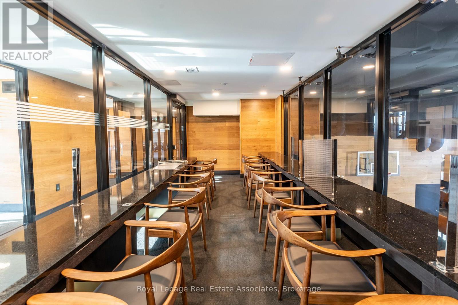 A long row of wooden chairs are lined up in a room with glass walls.