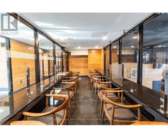 A long row of wooden chairs are lined up in a room with glass walls.