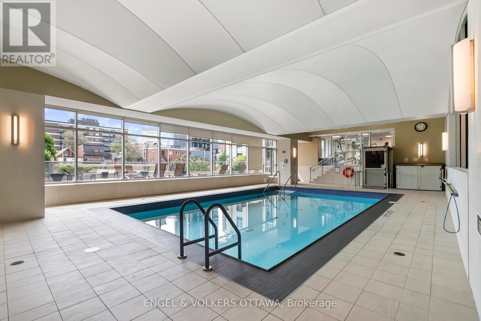 A large indoor swimming pool with a black edge and a black ladder.