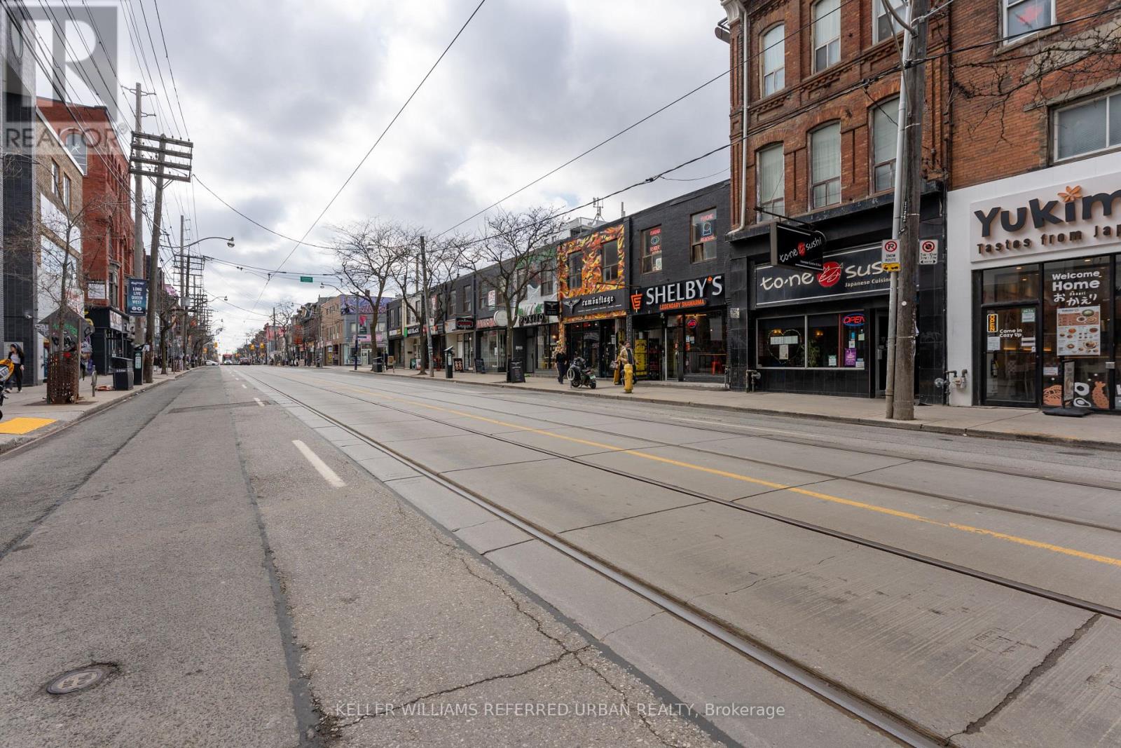 A street view of a city with buildings on both sides and a cloudy sky.