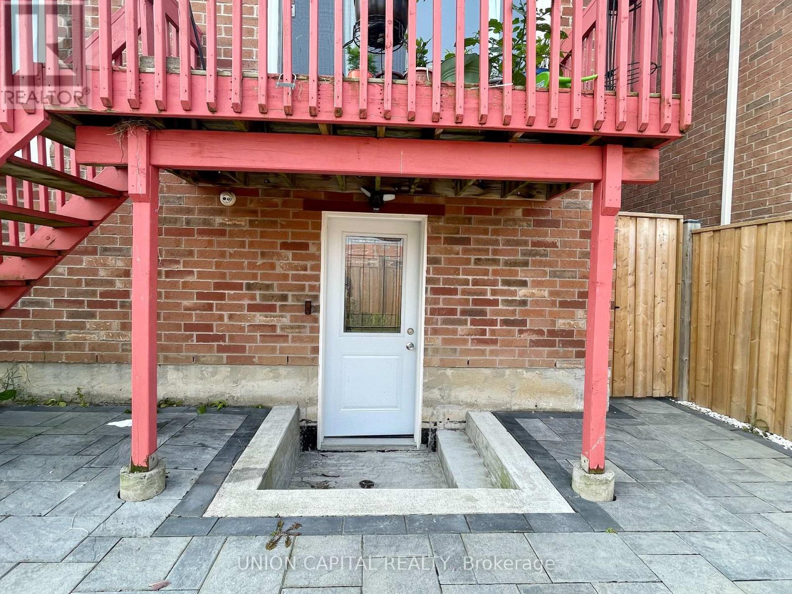 A white door is in a brick wall with a red railing above it.