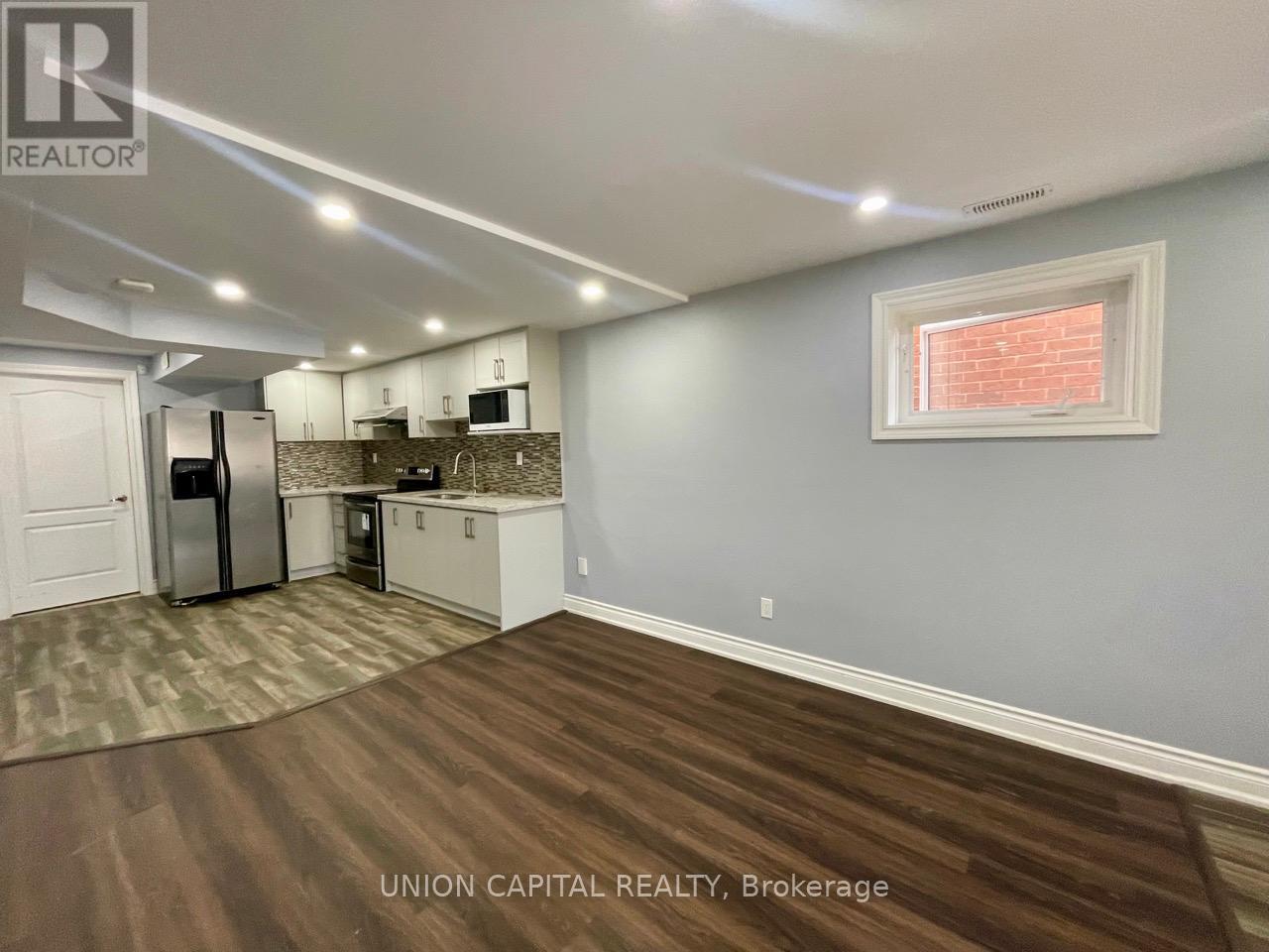 A kitchen with wood flooring and a window with blinds.