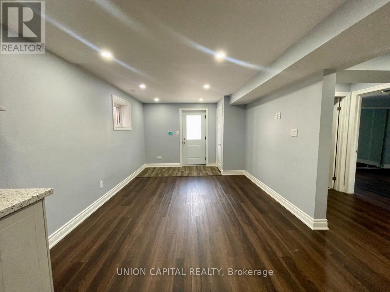 A spacious room with wood flooring and white walls, with a door at the end of the hallway.