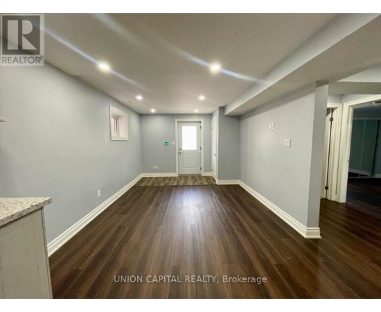 A spacious room with wood flooring and white walls, with a door at the end of the hallway.