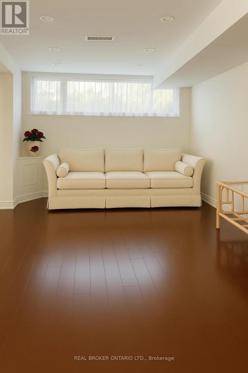 A white couch sits in a room with brown floors and a window with white curtains.