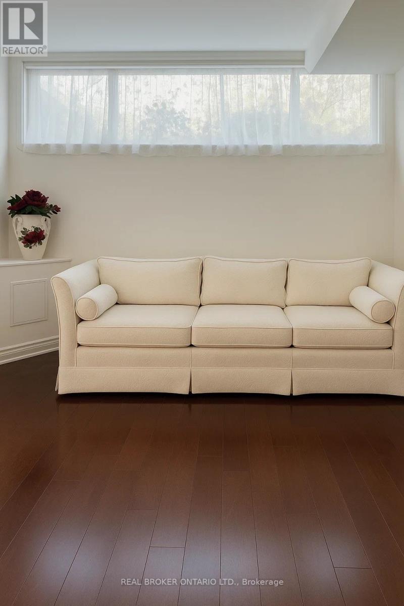 A white couch in a room with wooden flooring and a vase of flowers on a white dresser.