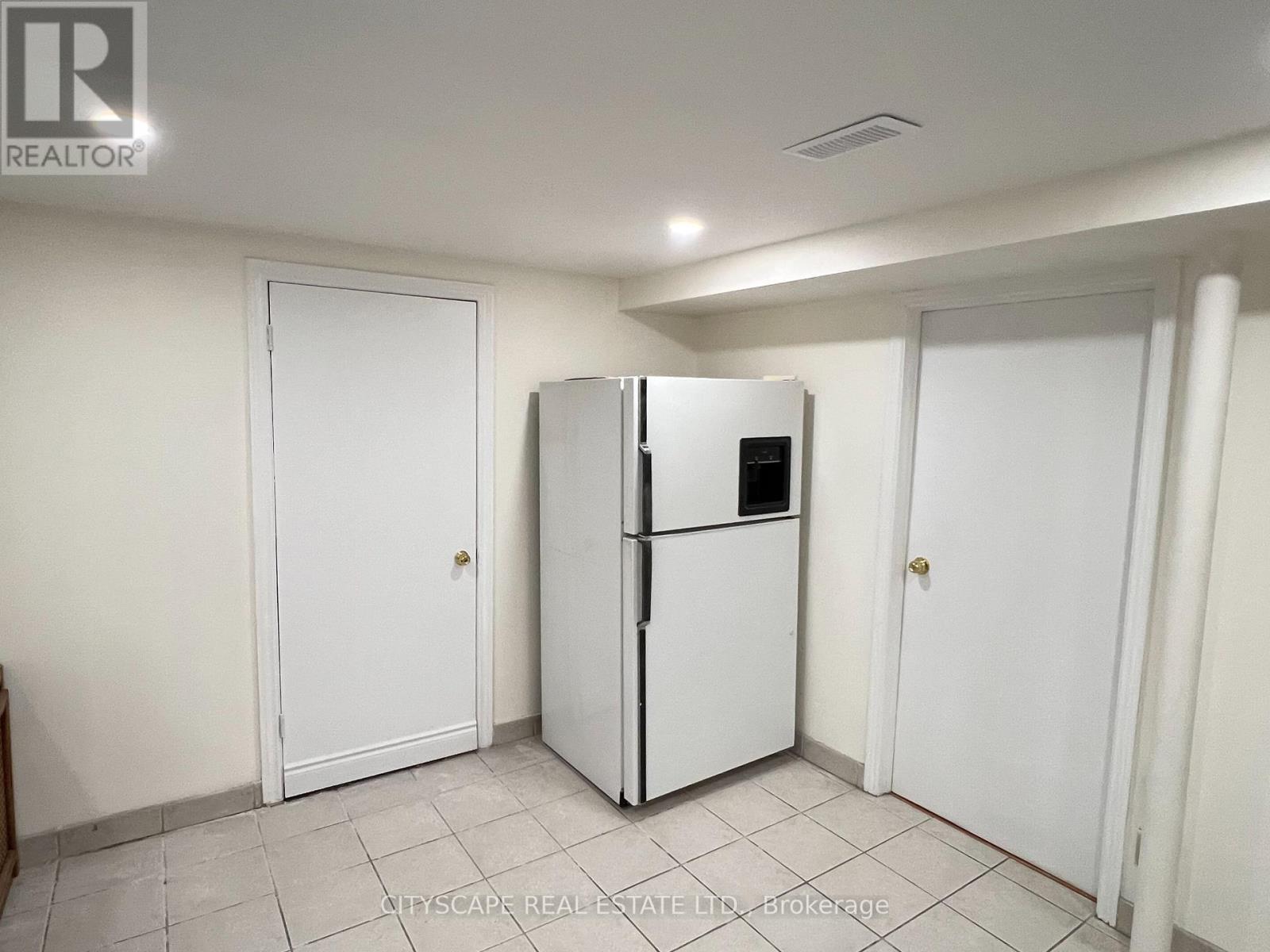 A white refrigerator is in the middle of a room with white walls and tile flooring.