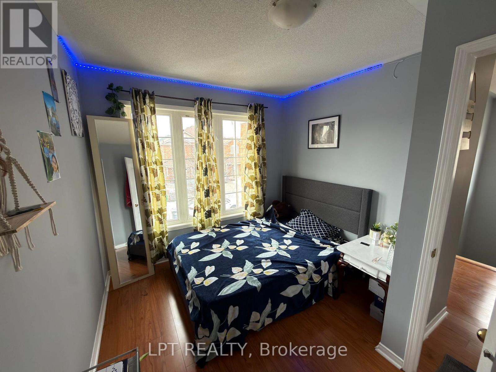 A bedroom with a bed in the center, a window with yellow curtains, and a picture on the wall.