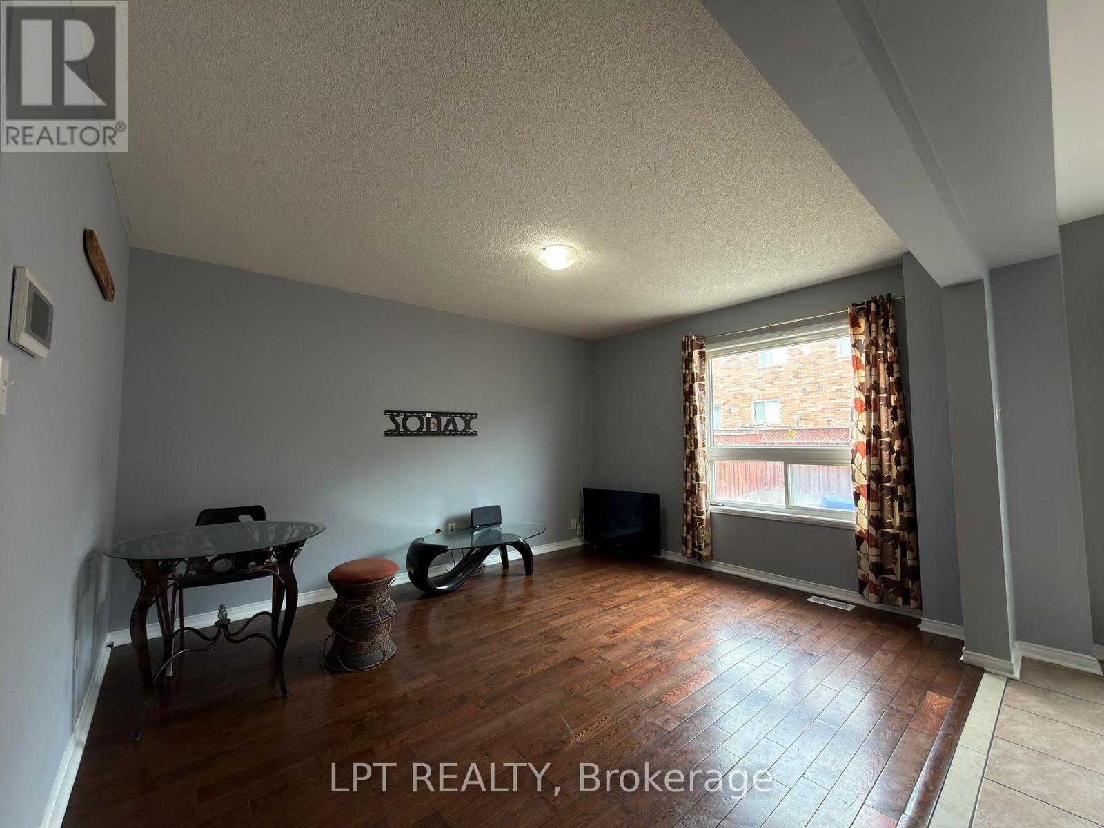 A living room with a glass table and chairs, a flat screen TV, and a window with curtains.