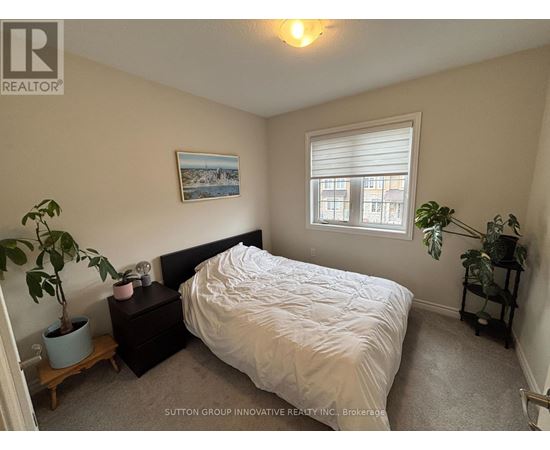 A bedroom with a bed, nightstand, and potted plant.