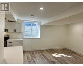 A real estate listing photo of a white kitchen with wood flooring and a window.