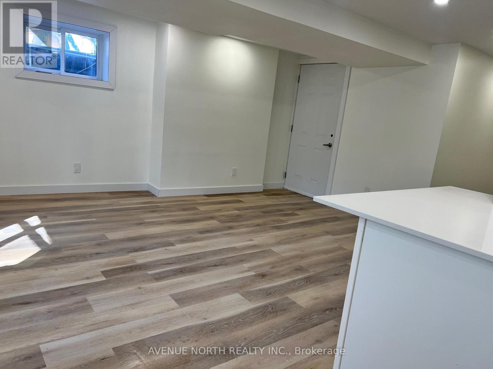 A room with wooden flooring and white walls, with a door and a window.